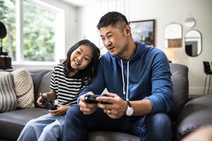 Two people (one adult, one kid) playing video games on the couch.