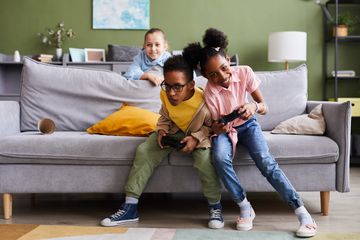 Kids playing video games at home together and fighting playfully.