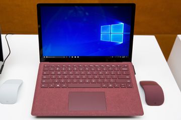 A screenshot of a red Microsoft Windows Surface laptop sitting on a white display. The laptop is sitting between two wireless mice: one white, one red.